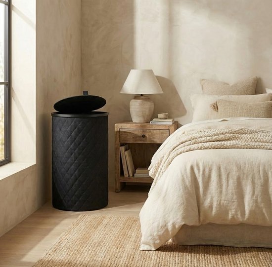 Zwarte, ronde wasmand met ruitpatroon naast een bed in slaapkamer.