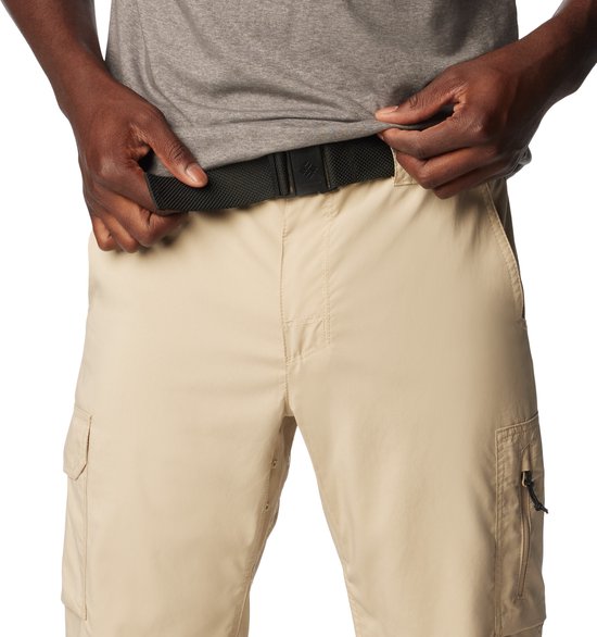 Man met grijze t-shirt, die zijn beige cargobroek met riem rechtzet. De broek heeft een ritszak op de dij.