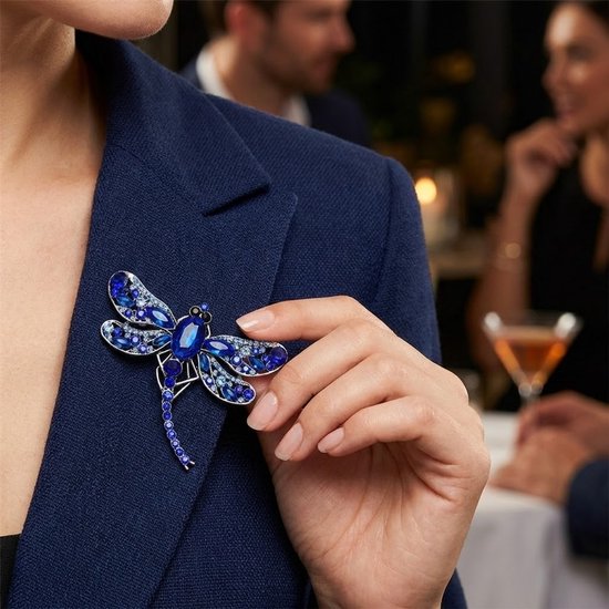 Blauwe libelle broche met zilverkleurig metaal en fonkelende facet geslepen stenen op een navy blazer.
