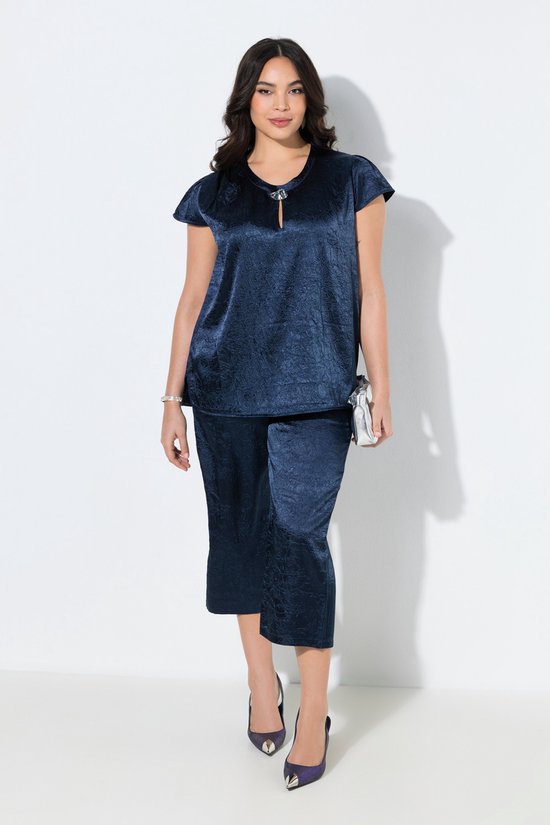Model in een marineblauwe outfit van culotte en top met textuur, met handtas en hakken.