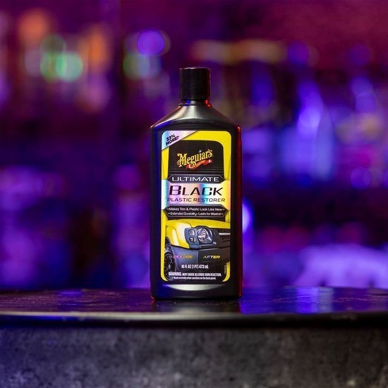 Fles Meguiar's Ultimate Black Plastic Restorer op een tafel met gekleurde lichten op de achtergrond.