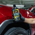 Hand in zwarte handschoen houdt Meguiar's Ultimate Black Plastic Restorer fles naast rode auto met zwarte wielkast.