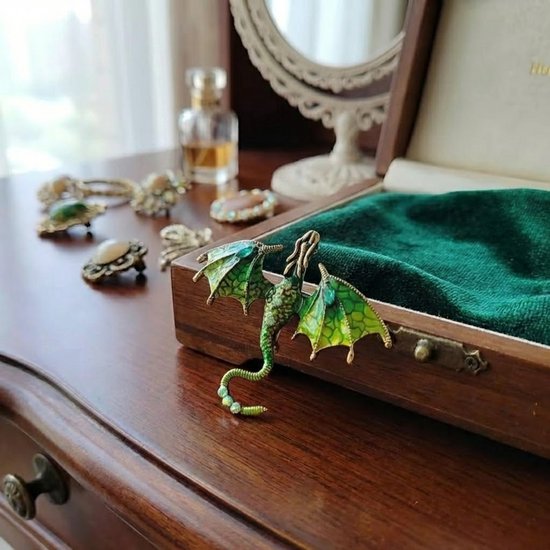 Groene drakenbroche met glinsterende vleugels op een houten kistje.