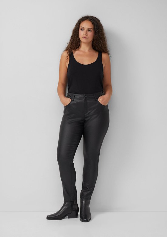 Model draagt een zwarte skinny broek met coating, gecombineerd met een zwarte top en laarzen.