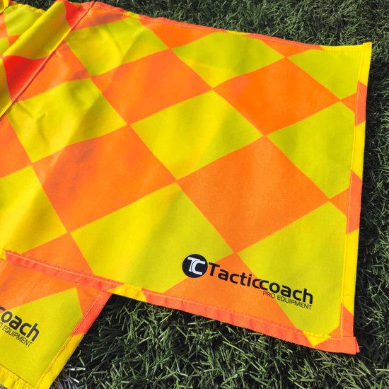 Grensrechtervlaggen met een ruitpatroon van geel en oranje, liggend op gras. De 'Tacticcoach PRO EQUIPMENT' logo is zichtbaar.