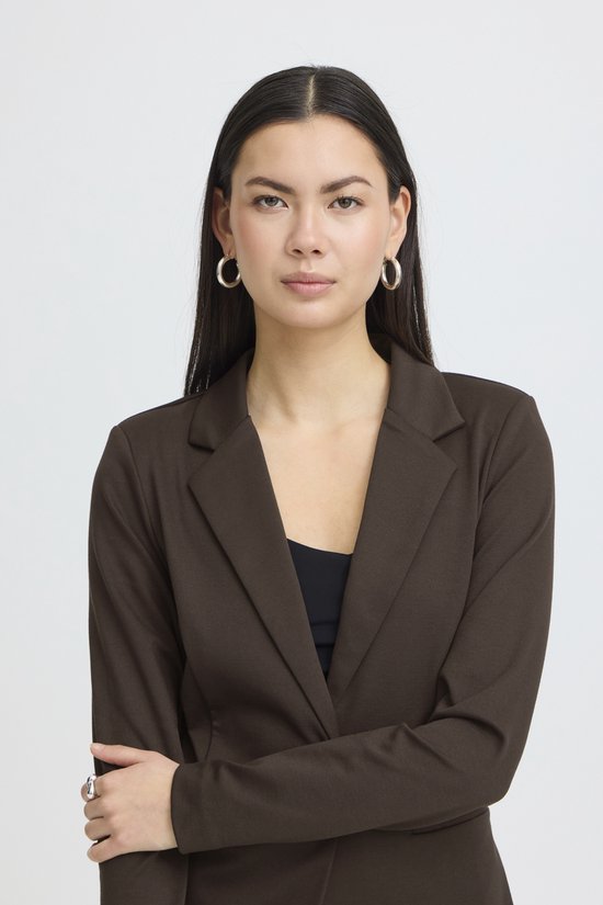 Vrouw, van voren gezien, met lange donkere haren, draagt bruine blazer over zwart topje.