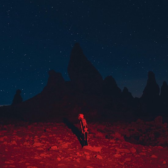 Un squelette éclairé en rouge se tient dans un désert rocheux sous un ciel étoilé.