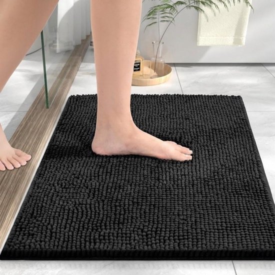 Een zwarte, pluizige chenille badmat, gefotografeerd vanuit het perspectief van iemand die erop stapt.