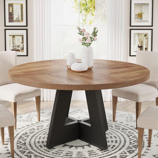 Table de salle à manger ronde avec plateau à chevrons en bois et base métallique noire en forme de A, décorée de vases, avec des chaises autour.