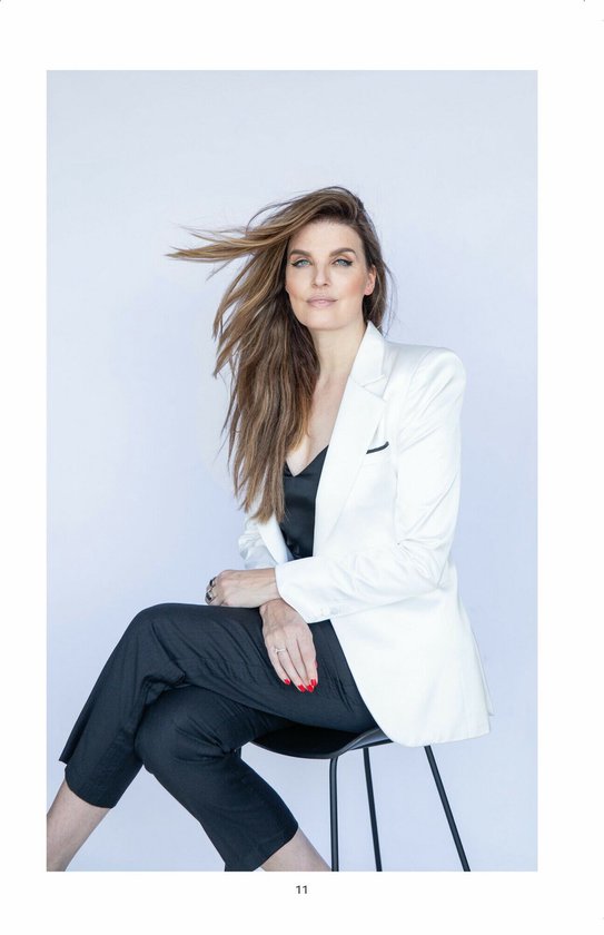 Model met lang bruin haar, gekleed in een zwarte top en zwarte broek met een witte blazer.