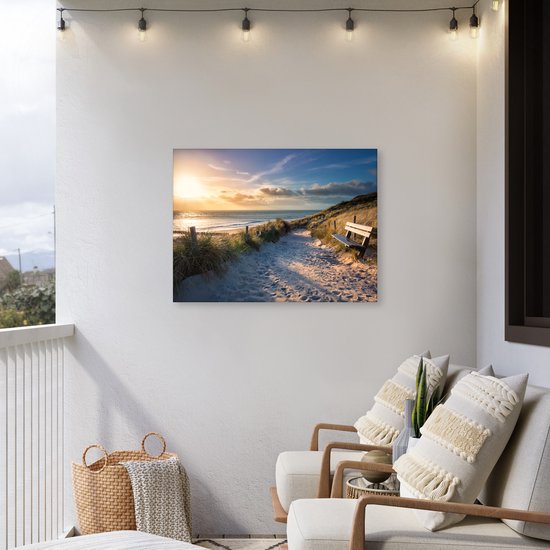Zonsondergang op een strand met duinen, een zandpad, houten hekken en een bankje. Hangt aan een muur op een balkon met stoelen.