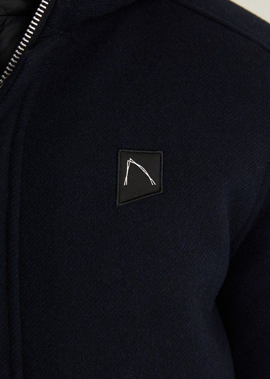 Detail van donkerblauwe wollen stof met logo-badge op de borst.