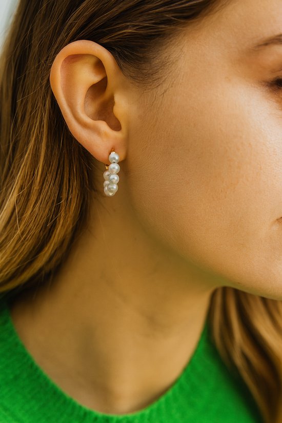 Oorhangers met meerdere witte parels aan een goudkleurig oorstukje, gedragen door een model.