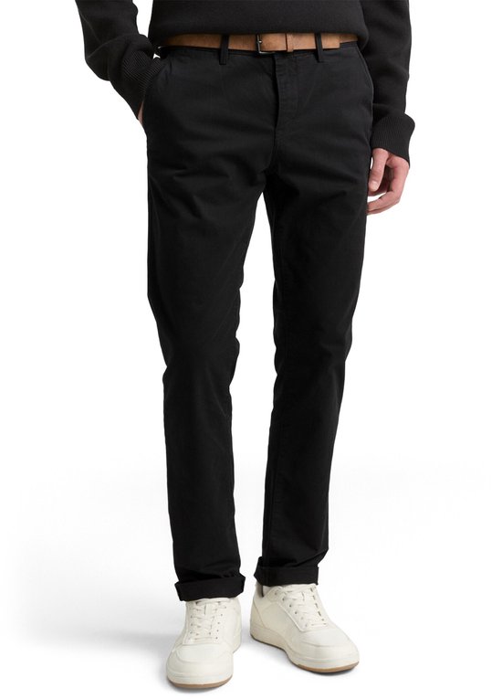 Man van voren, draagt een zwarte chino met bruine riem, witte trui en witte sneakers.