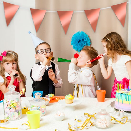 Des enfants avec des chapeaux de fête et des trompettes soufflent la fête, autour d'un gâteau avec des bougies.