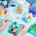 Handen die een groen organzazakje met kerstkransjes sluiten. Andere zakjes met parels, gouden ballen en knuffels liggen verspreid.