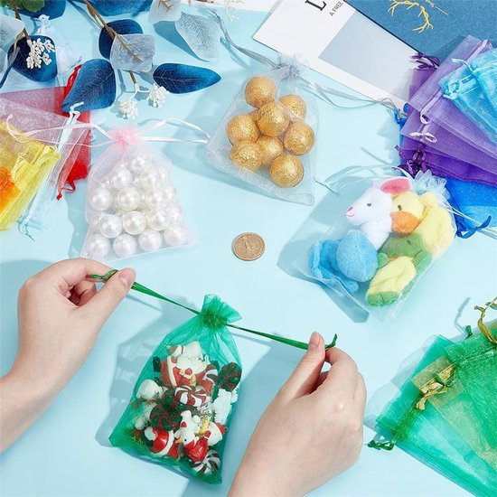 Handen die een groen organzazakje met kerstkransjes sluiten. Andere zakjes met parels, gouden ballen en knuffels liggen verspreid.