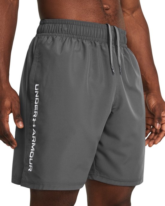 Grijze sportbroek van Under Armour met witte tekst op de zijkant, gedragen door een man.