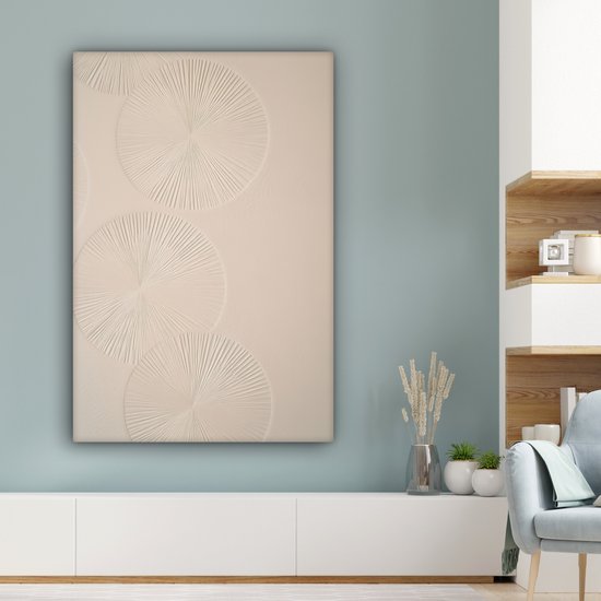 Beige canvas met cirkels in reliëf, hangend boven een witte kast in een woonkamer met blauwe muur.