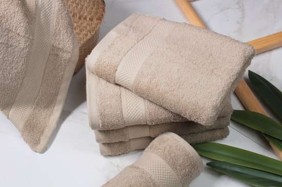 Une pile de serviettes beige taupe avec une bande décorative, à côté d'un panier et de feuilles vertes.