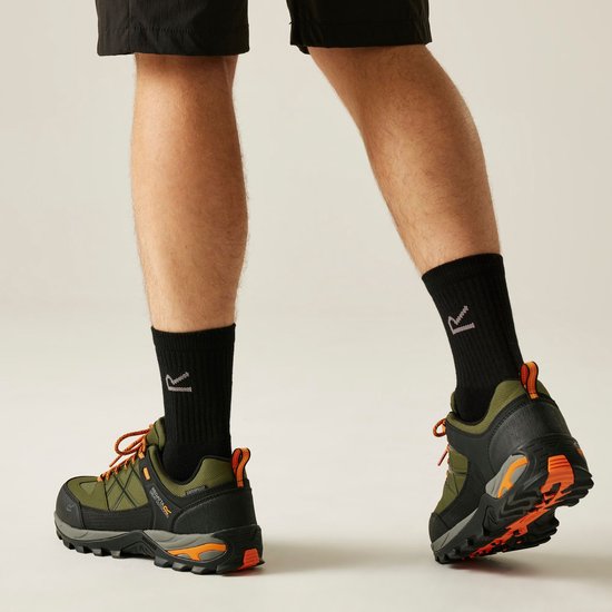 Homme portant des chaussettes noires et des chaussures de randonnée vertes à lacets orange, marchant en extérieur.