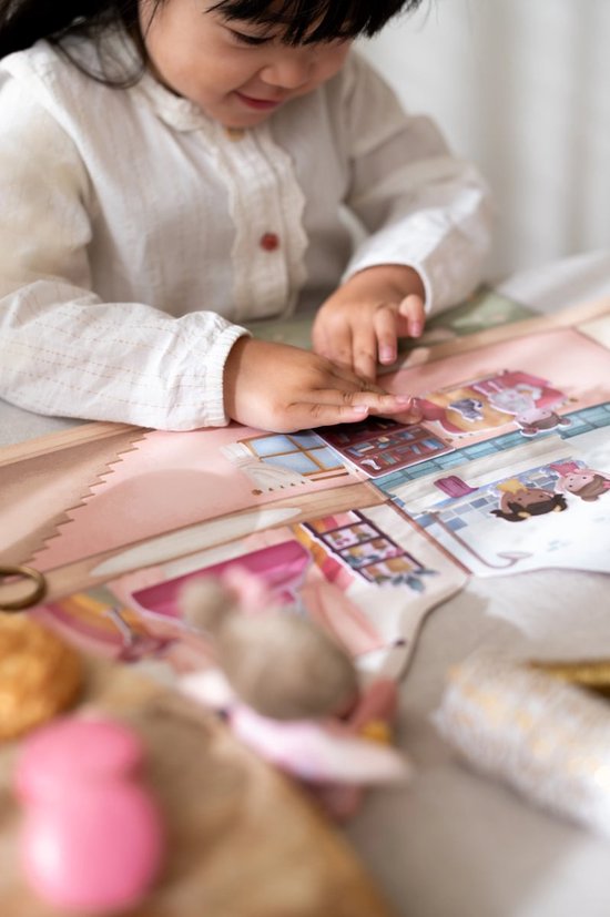 Meisje plakt stickers op een kartonnen speelset met kamers, meubels en poppetjes.