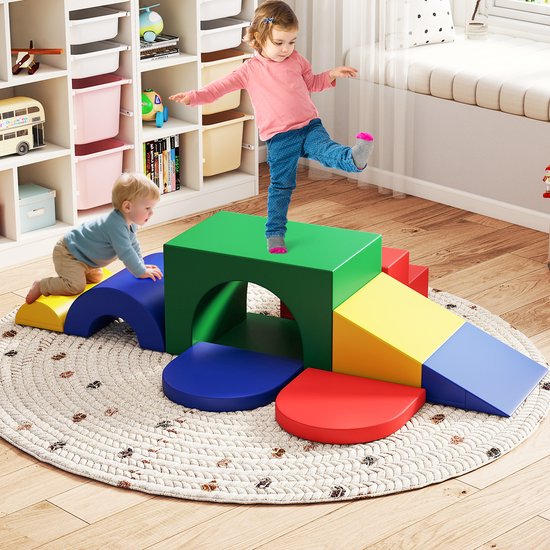 Kinderen spelen op veelkleurige schuimblokken (groen, rood, geel, blauw) in een kinderkamer met een ronde mat.