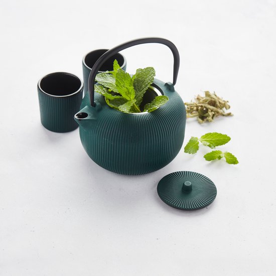 Donkergroene gietijzeren theepot met geribbelde textuur, gevuld met verse munt, met twee zwarte kopjes ernaast.