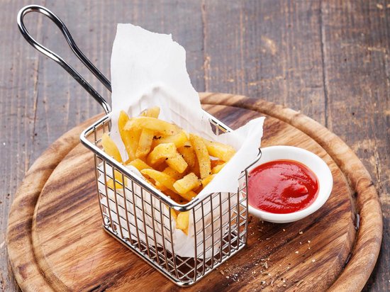 Een vierkant RVS frietmandje, gevuld met frietjes en op een houten plank met ketchup.