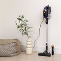 Blauwe en oranje steelstofzuiger met accessoires, naast een vaas en poef in een woonkamer.