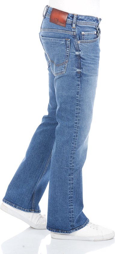 Zijaanzicht van een man in een bootcut blauwe spijkerbroek met witte sneakers.