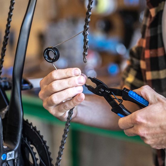 Gros plan d'une personne utilisant une pince à chaîne bleue pour retirer une chaîne de vélo.