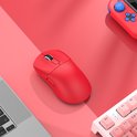 Een rode gaming muis op een bureau naast een laptop en een roze toetsenbord.
