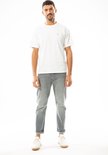 Man in een witte T-shirt met een klein blauw logo. Grijze jeans.