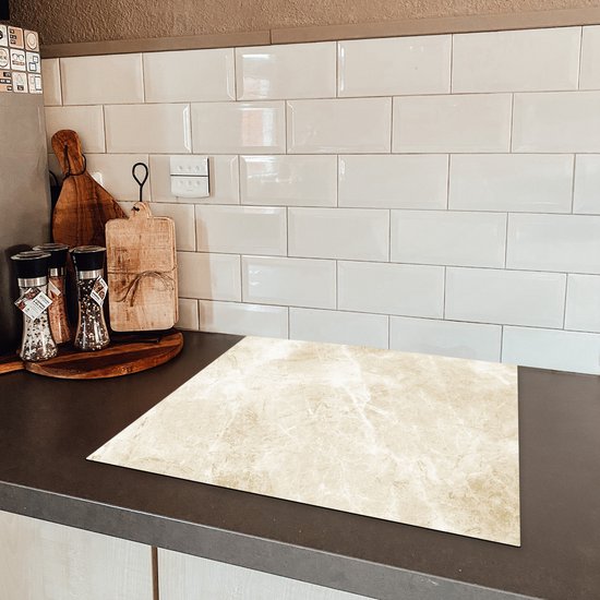 Beige marmerprint inductiebeschermer op een aanrecht naast een inductiekookplaat.
