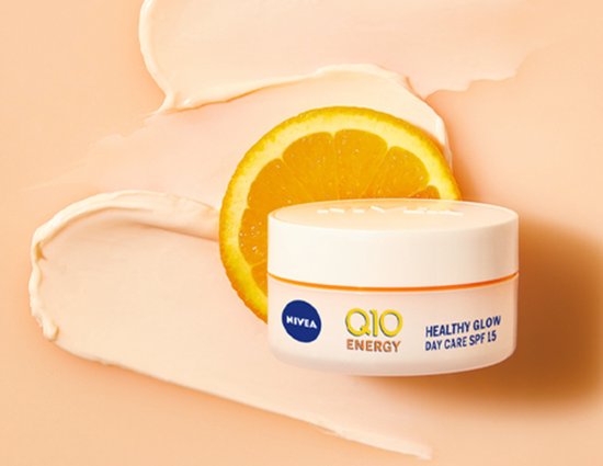 Nivea Q10 Energy Healthy Glow potje crème met een partje sinaasappel, omringd door crèmekleurige vegen.