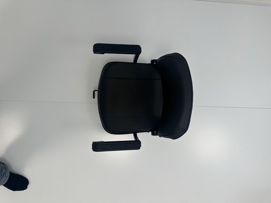 Zwarte zitting met armleuningen van een scootmobiel, gefotografeerd van bovenaf.