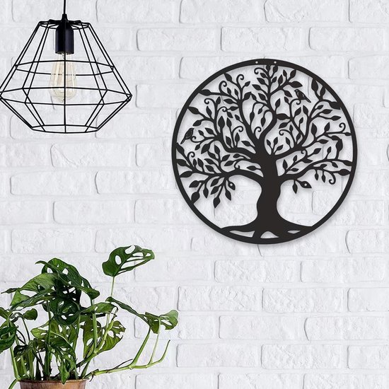 L'arbre de vie en métal noir est suspendu à un mur de briques à côté d'une plante et d'une lampe géométrique.