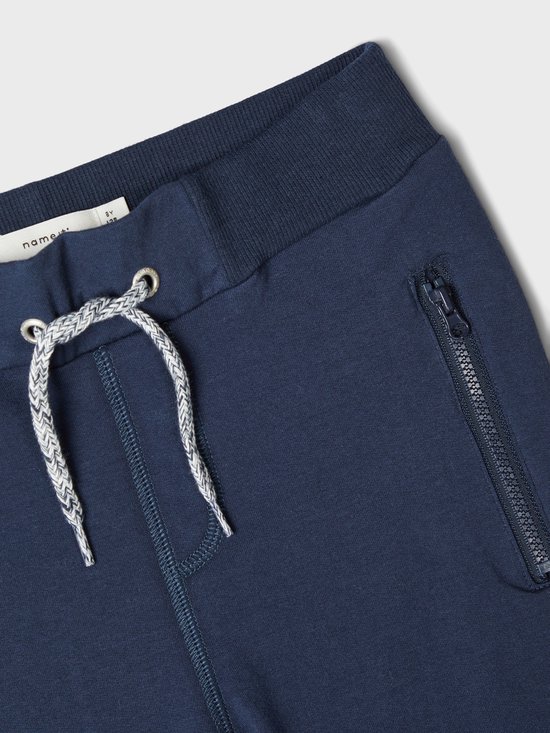 Detail van donkerblauwe joggingbroek met trekkoord en ritszak.