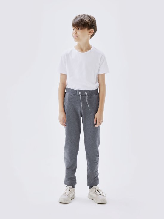 Jongen in grijze joggingbroek, wit t-shirt en lichte sneakers.
