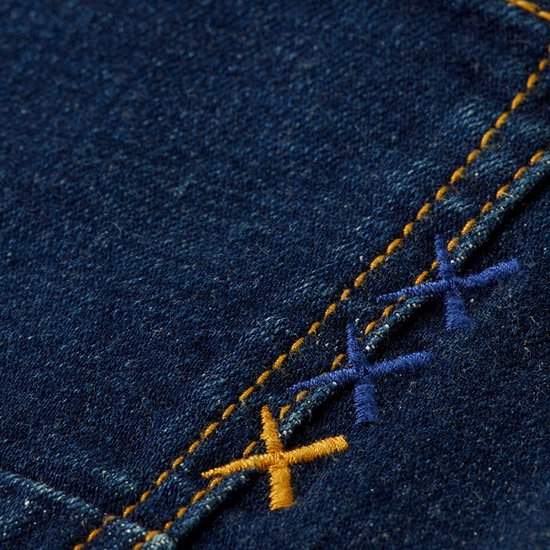 Detail van donkerblauwe jeans met gele en blauwe kruisstiksels.