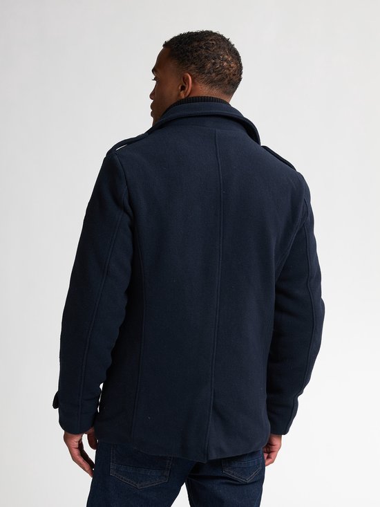 Achterkant van een man met donkerblauwe peacoat, jeans en bruine schoenen.