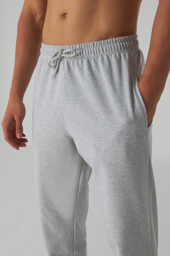 Man met de hand in de zak van een grijze joggingbroek, elastische tailleband met trekkoord.