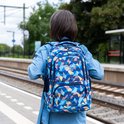 Van achteren gezien, meisje met spijkerjas draagt blauwe rugzak met geometrisch patroon op perron.