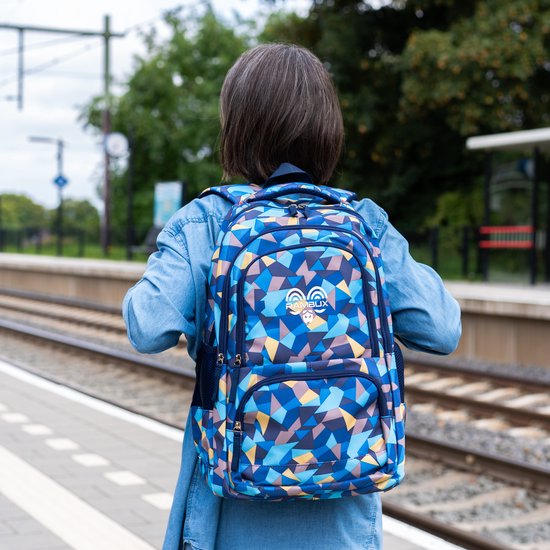 Van achteren gezien, meisje met spijkerjas draagt blauwe rugzak met geometrisch patroon op perron.
