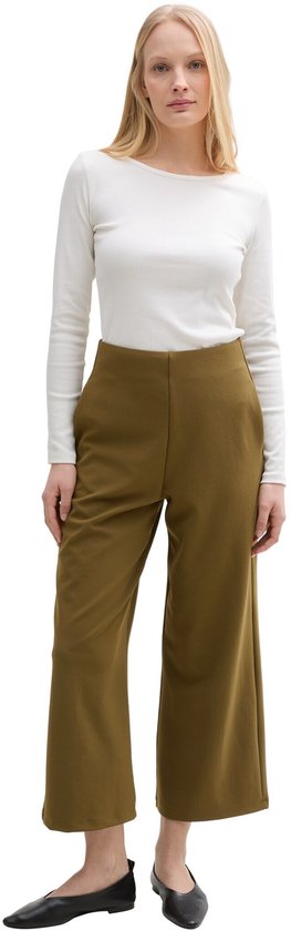 Model draagt een olijfgroene culotte met wijde pijpen en een hoge taille. Ze draagt een witte top met lange mouwen.
