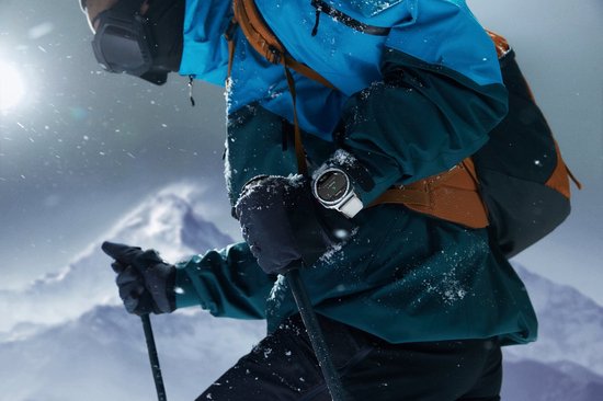 Persoon in wintersportkleding met een smartwatch om de pols, skiënd in besneeuwde bergen.