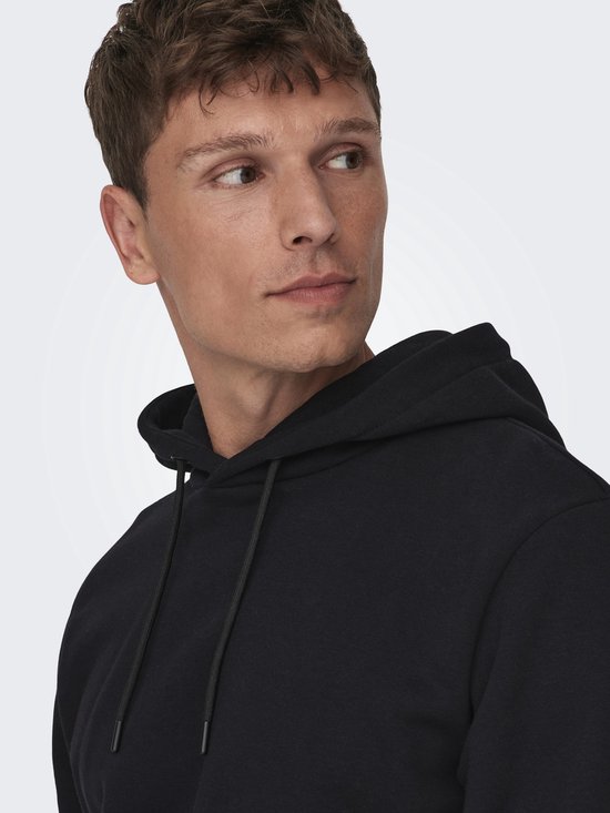 Close-up van een man met donker haar die een zwarte hoodie draagt.
