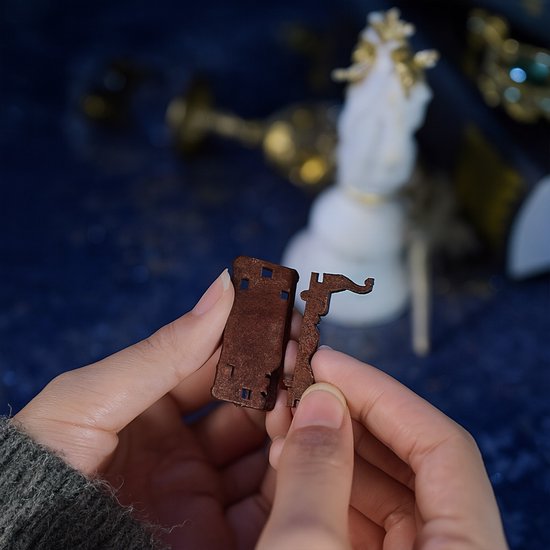 Handen houden twee bruine, houten onderdelen van een miniatuur vast, klaar voor montage.