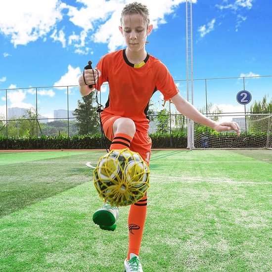 Jongen in oranje shirt met bal aan elastiek, traint op groen veld.